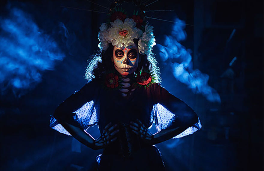A woman dressed in a festive Day of the Dead costume, enhanced with illuminated Halloween gear