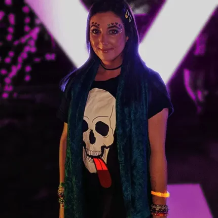 Girl at rave wearing face make up and skull t-shirt with tongue that is lighting up bright red at dark festival