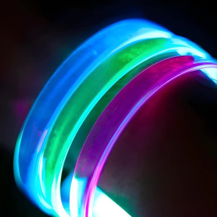 Close up image of clear LED bracelets when turned on, blue, green, and pink LED bracelets on wrist