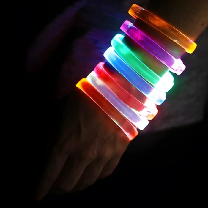 Someone wearing 7 different LED bracelets on their arm, all lighting up in different colors