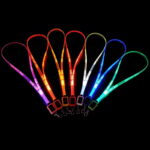 Seven LED lanyards lined up in a dark room glowing pink, orange, yellow, red, white, blue, and green with custom logo laser engraved onto them