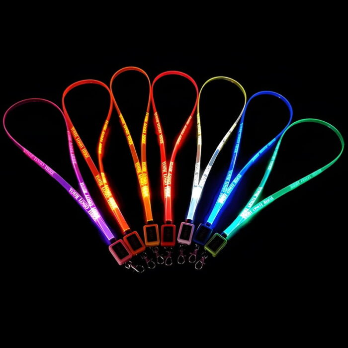 Seven LED lanyards lined up in a dark room glowing pink, orange, yellow, red, white, blue, and green with custom logo laser engraved onto them