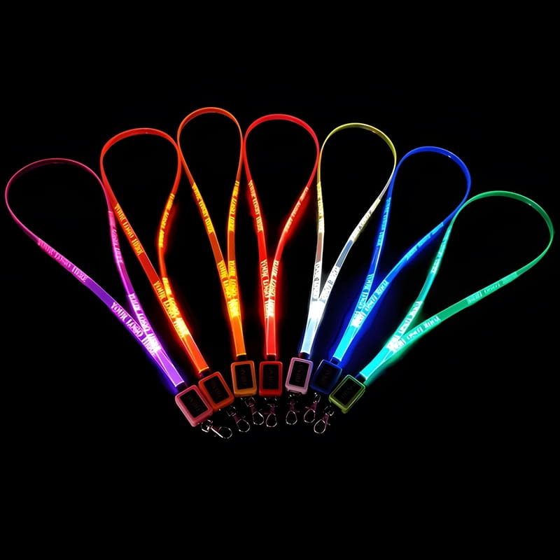 Seven LED lanyards lined up in a dark room glowing pink, orange, yellow, red, white, blue, and green with custom logo laser engraved onto them