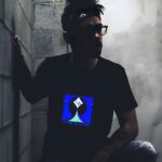 Man kneeling leaning against cinder block wall in dark basement while light up t-shirt design illuminates the room