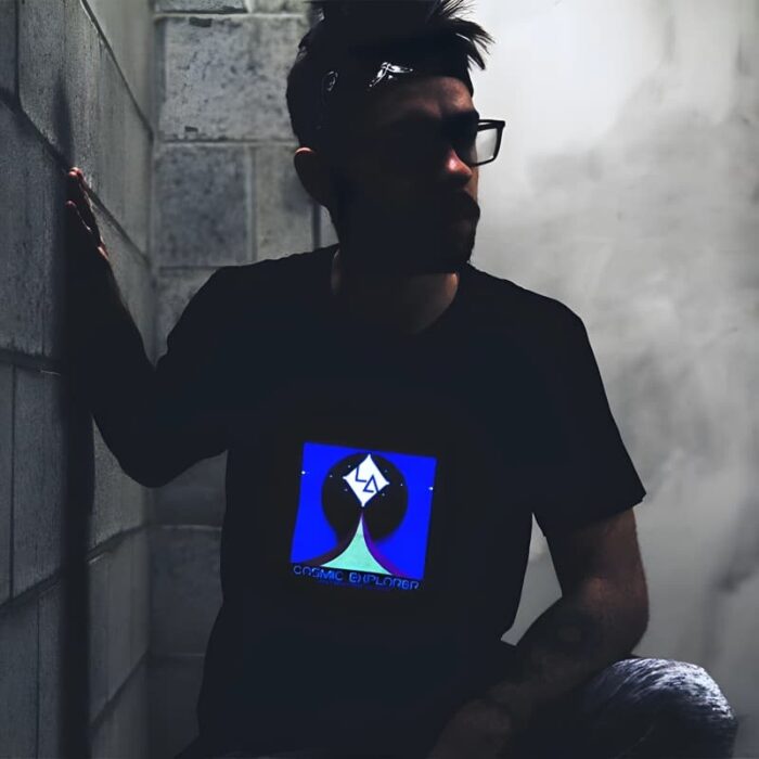Man kneeling leaning against cinder block wall in dark basement while light up t-shirt design illuminates the room