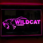 Wildcat text and logo laser engraved onto neon acrylic sign lighting up bright pink in dark room