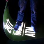 Person standing on glowing sign that they are also holding in their hand to show the flexibility and durability of the material