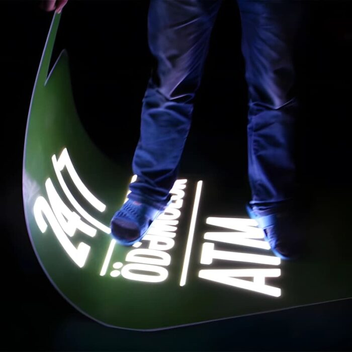 Person standing on glowing sign that they are also holding in their hand to show the flexibility and durability of the material