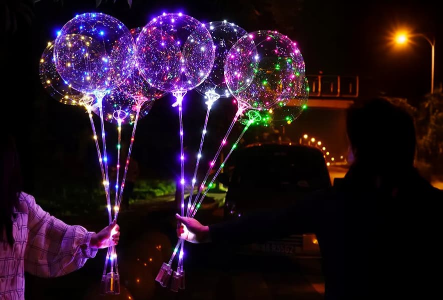 Two people hold illuminated clear balloons, creating a festive atmosphere with glowing lights
