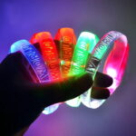 Hand holding five different colored custom LED bracelets lighting up bright neon colors