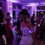 Bride dancing at wedding with two different LED bracelets on each wrist while other guests re dancing with custom led bracelets shining bright on their arms
