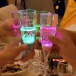 A group of four LED champagne glasses in a cheers position lighting up bright green and pink