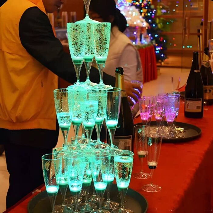 Three tiers of LED champagne glasses stacked up high on a table illuminating bright green