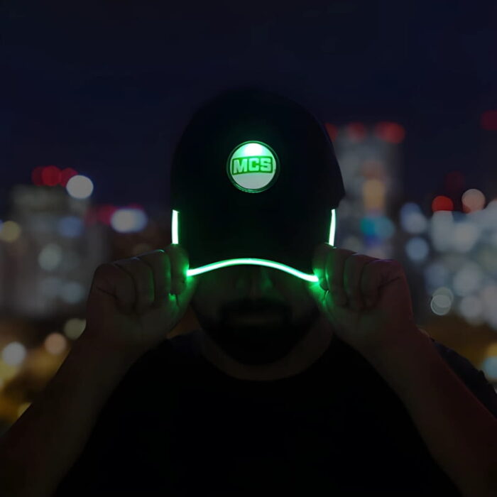 A man in a green hat featuring a glowing logo, with the brim brightly lit in green.