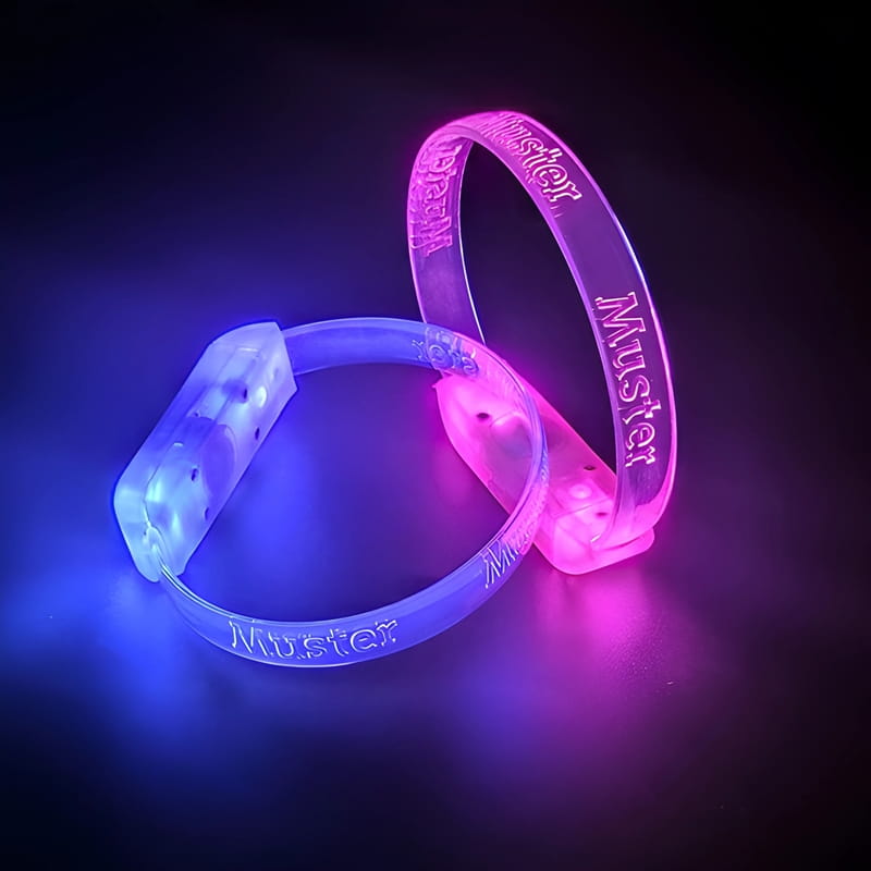 Two bracelets with custom engraved Muster logo lighting up bright blue and hot pink in dark room