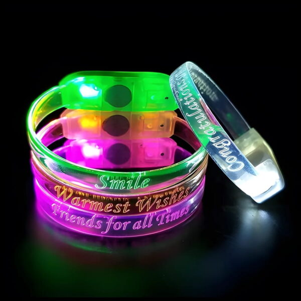 Three custom LED bracelets stacked up with another white LED bracelet leaning against it in a dark room, all glowing in LED colors