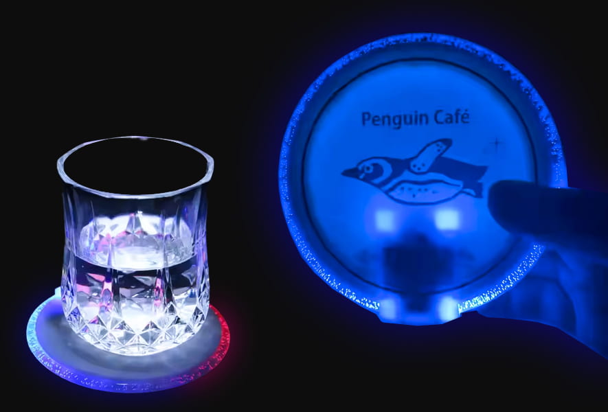 A glass featuring a penguin design sits on a light-up coaster, illuminating the surface beneath it