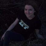 Smiling girl posing in dark while sorority greek letters are lighting up on her shirt