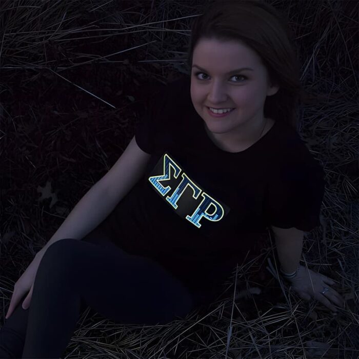 Smiling girl posing in dark while sorority greek letters are lighting up on her shirt