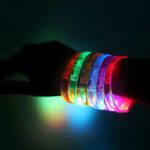 A close-up of a person wearing 6 brightly lit up bracelets, featuring multiple LED glowing colors.