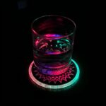 A glass of water illuminated by a colorful light from a light-up drink coaster beneath it