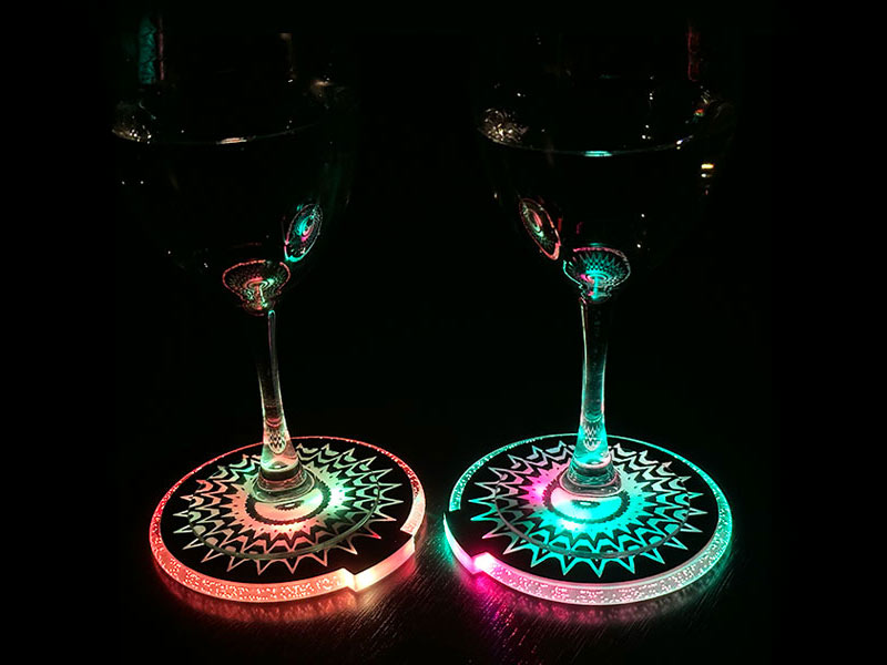 Two wine glasses illuminated by colorful LED lights, resting on light-up drink coasters