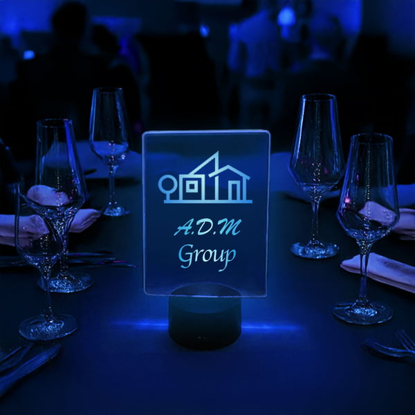 A blue lighted acrylic sign on a table reads "a d m group," highlighting the brand's identity