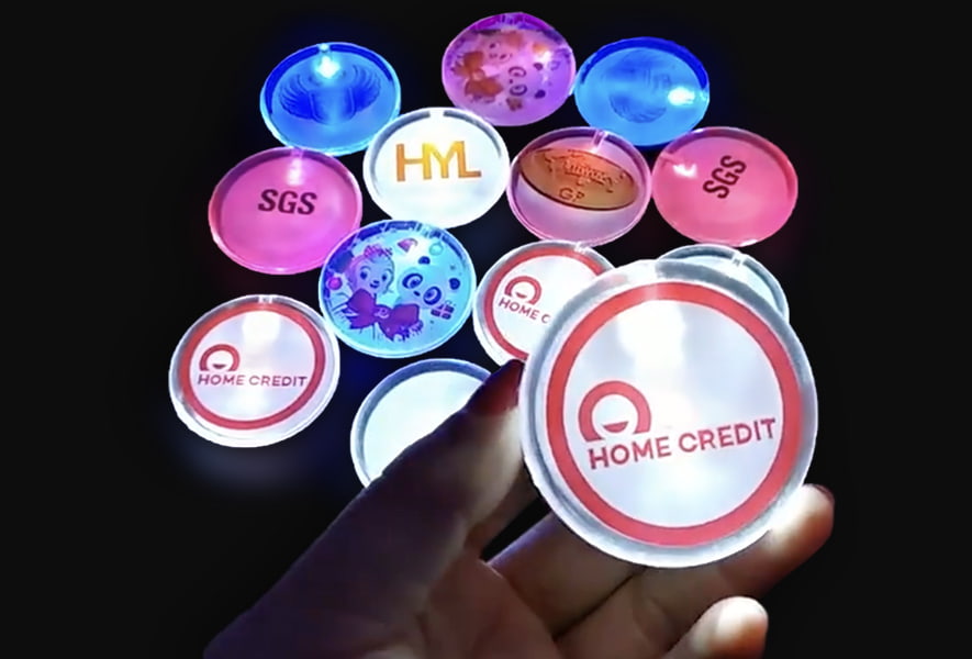 A person holds a round LED light up pin featuring a logo, showcasing it prominently in their hand