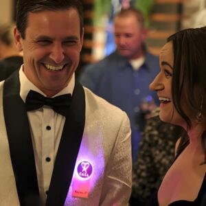 A man and woman in formal wear laugh together, illuminated by colorful LED light pins on their outfits.