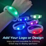 A hand holds four light up silicone wristbands in red, blue, purple, and green, showcasing different logos.