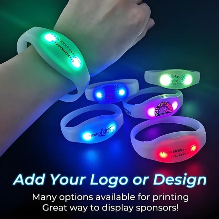 A hand holds four light up silicone wristbands in red, blue, purple, and green, showcasing different logos.