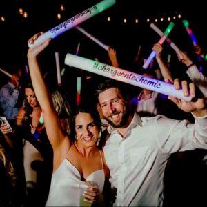 Happy couple at wedding dancing with guests waving color changing LED foam sticks in the air