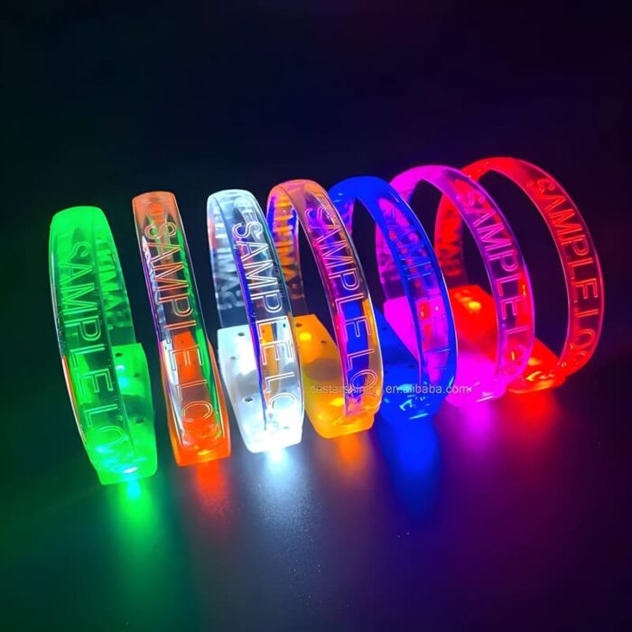 Seven custom LED bracelets with sample logo laser engraved lined up in a row showing each color, green, orange, white, yellow, blue, pink and red
