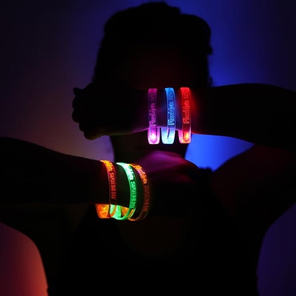 Darkly silhouetted person wearing six led bracelets with Flashion Statement logo, holding arms in front of face to show off the bright illuminating colors