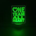Custom engraved acrylic LED sign with "One Team All Heart" text, illuminated by a green LED base.