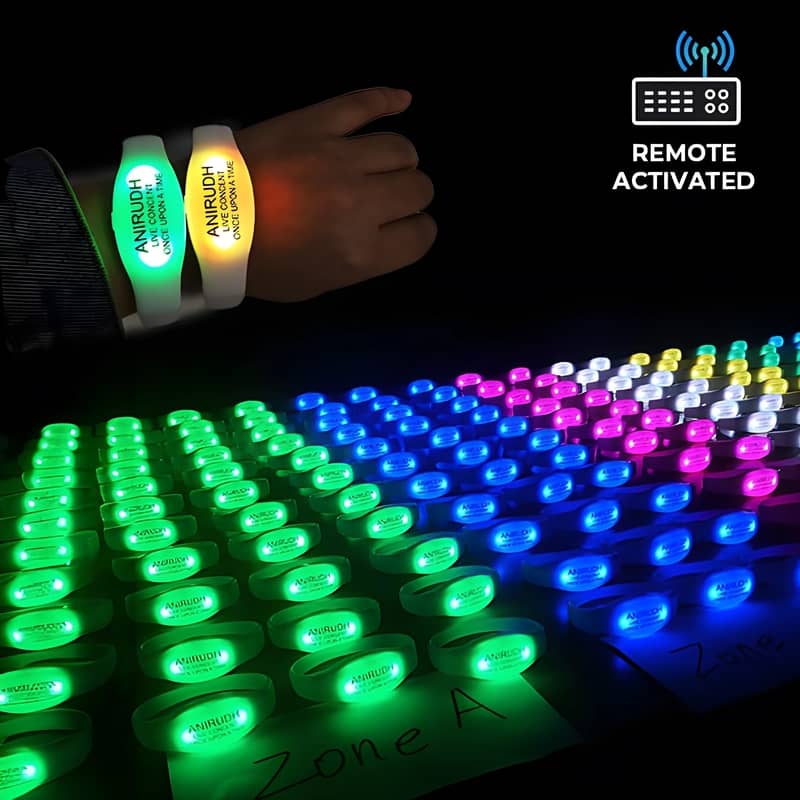 Close up of wrist wearing two custom silicone LED bracelets shown in front of table of LED bracelets separated into different zones and colors