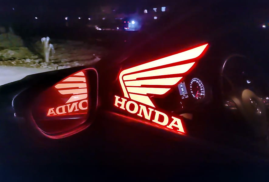 A vehicle displaying an illuminated car sticker on the windshield with a red Honda Logo