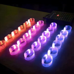 four groups of light up wristbands sitting on table with each row illuminating a different color due to the RFID remote controller to the right of the bracelets