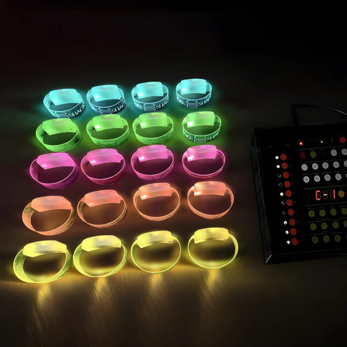 5 rows of LED wristbands lined up in dark room on desk with remote control lighting each row a different color from top to bottom: cyan, green, pink, orange and yellow