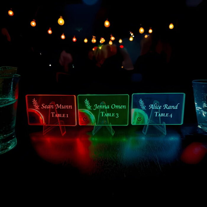 Three bright acrylic place cards with names and table numbers displayed on a table at an event