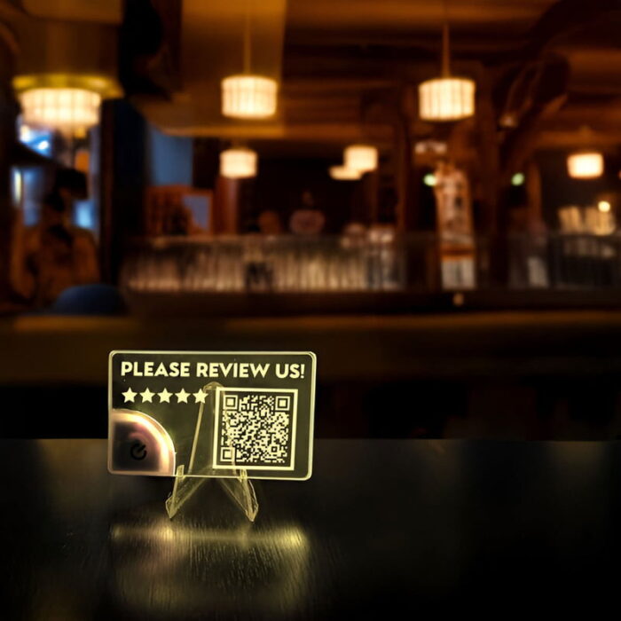 A bright acrylic card displays "Please Review Us" alongside a QR code, inviting restaurant customers to leave feedback