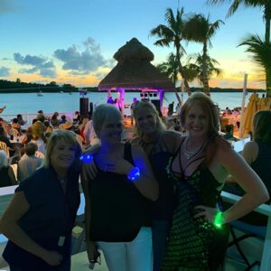 Four women wearing different colored LED bracelets lighting up in front of stage at concert on the water