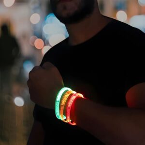 Man in beard wearing black shirt with arm lifted to show three laser engraved LED bracelets glowing green, orange and red