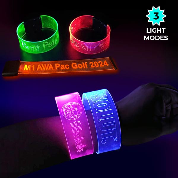 close up of wrist wearing two large glowing bracelets with engraved designs in front of other custom LED wristbands in neon colors