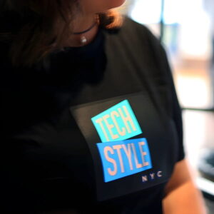 Close up of woman wearing tightly fitted light up shirt with Tech Style logo illuminating brightly