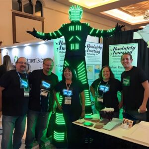 A group of people in LED light-up t-shirts posing beside a giant robot at a corporate tradeshow