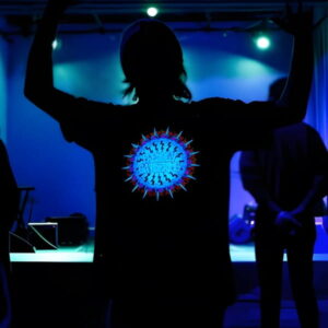 Silhouette of guy in front of stage holding his hands up with a Frendly Gathering custom light up shirt illuminating