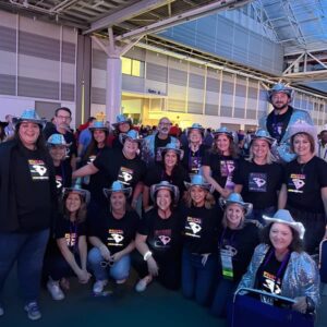 Large group of people wearing rhinestone cowboy hats posing with their light up shirts at a conference