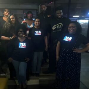 Group of African Americans wearing light up shirts in dark studio setting with logo glowing