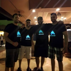 Four men in black shirts with blue LED lights, standing together with arms around each other, smiling and posing
